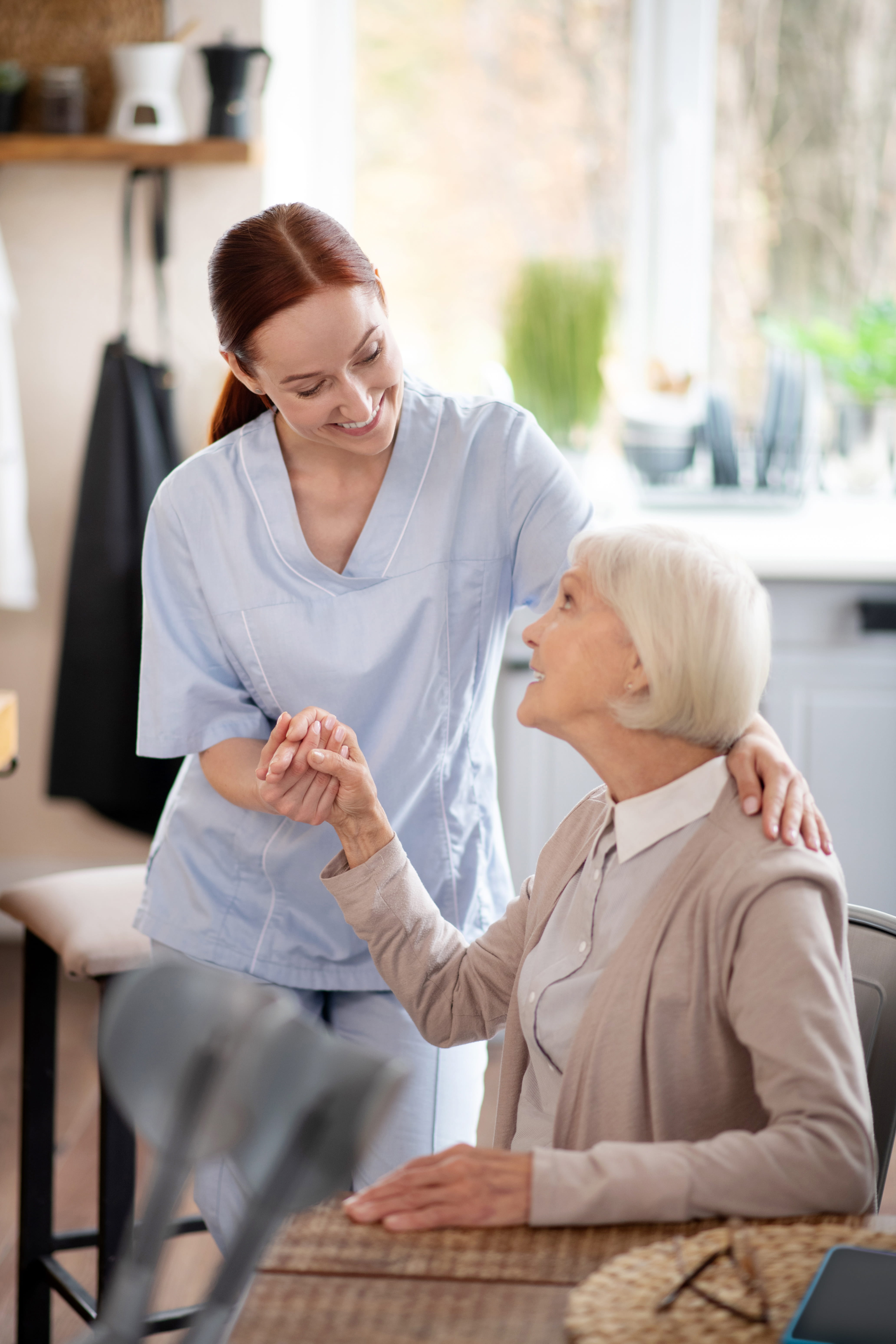 A female caregiver helping a female resident stand up from the dining table chair.