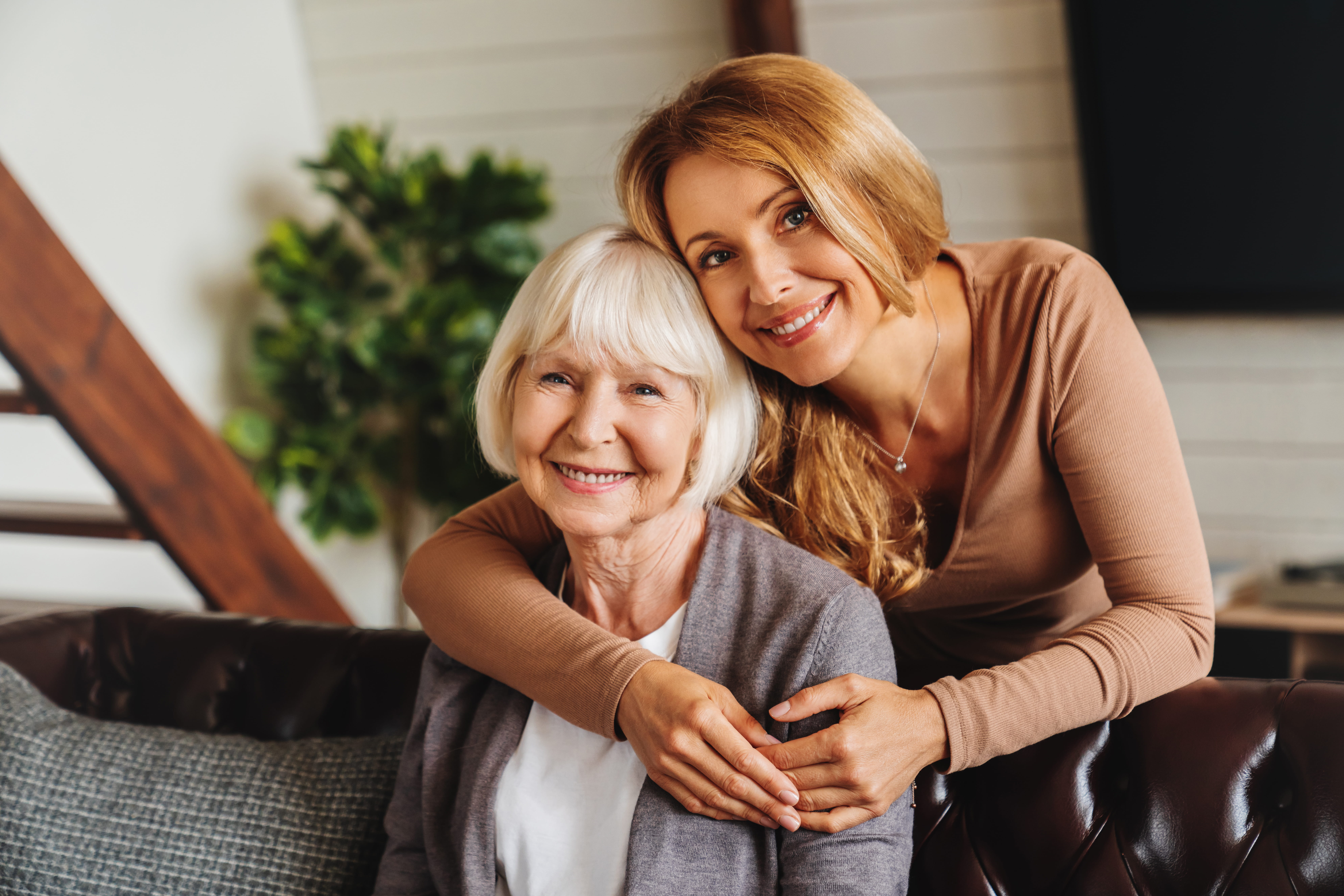 Adult daughter standing over and hugging senior mother.