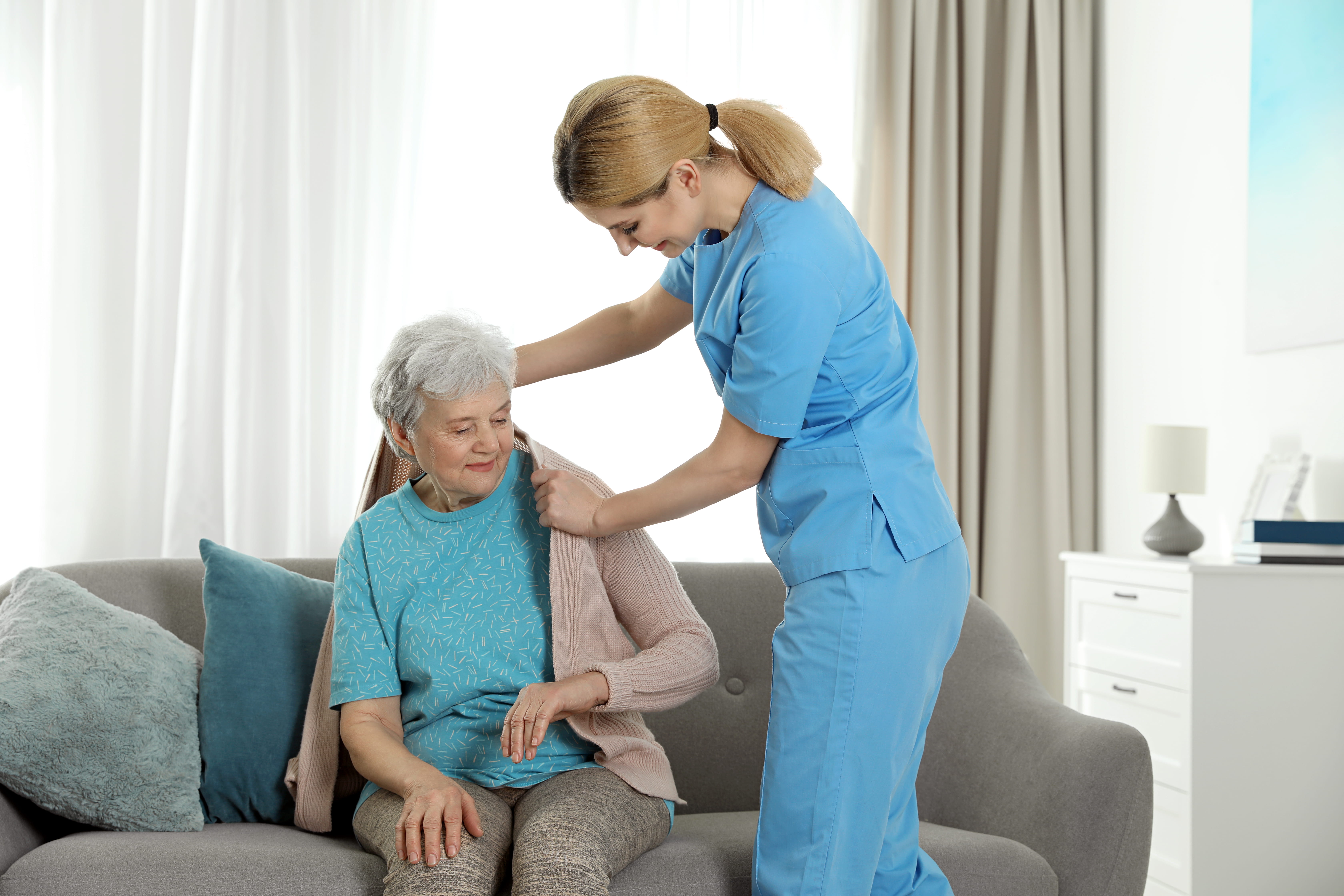 Caregiver helping put on coat for senior female resident.