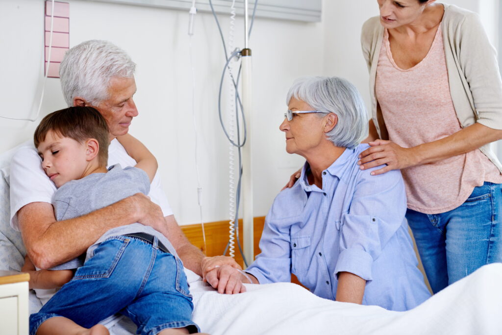 Senior male patient in hospital bed surrounded by family.