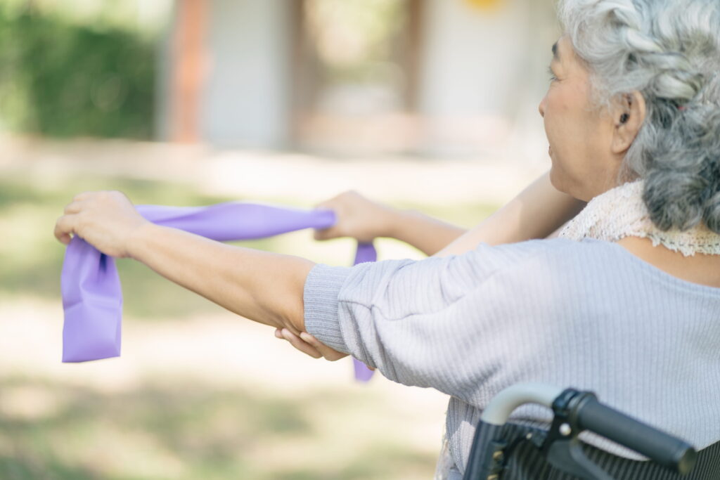 Senior woman exercising with band outdoors.